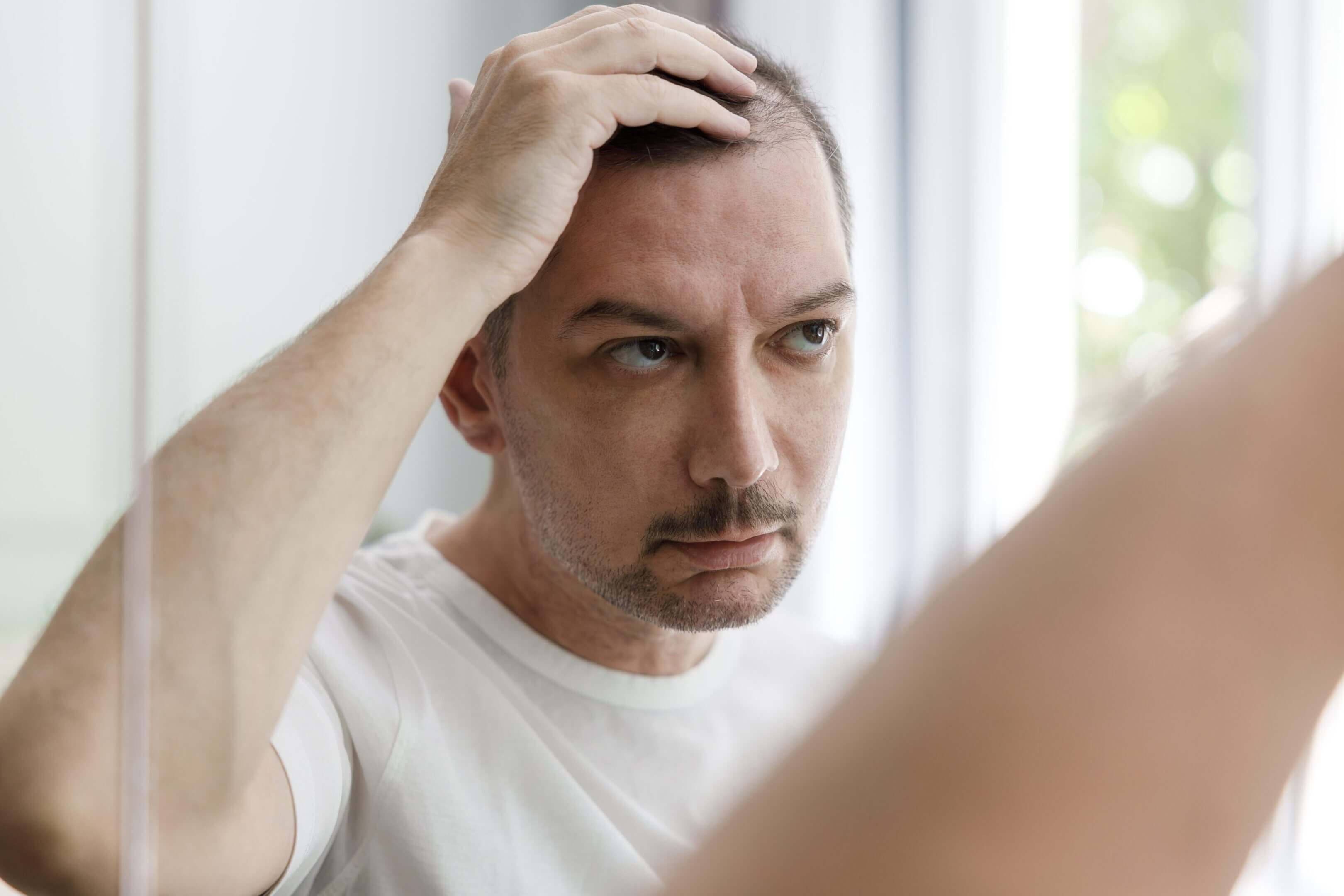 Man examining hair in bathroom mirror.