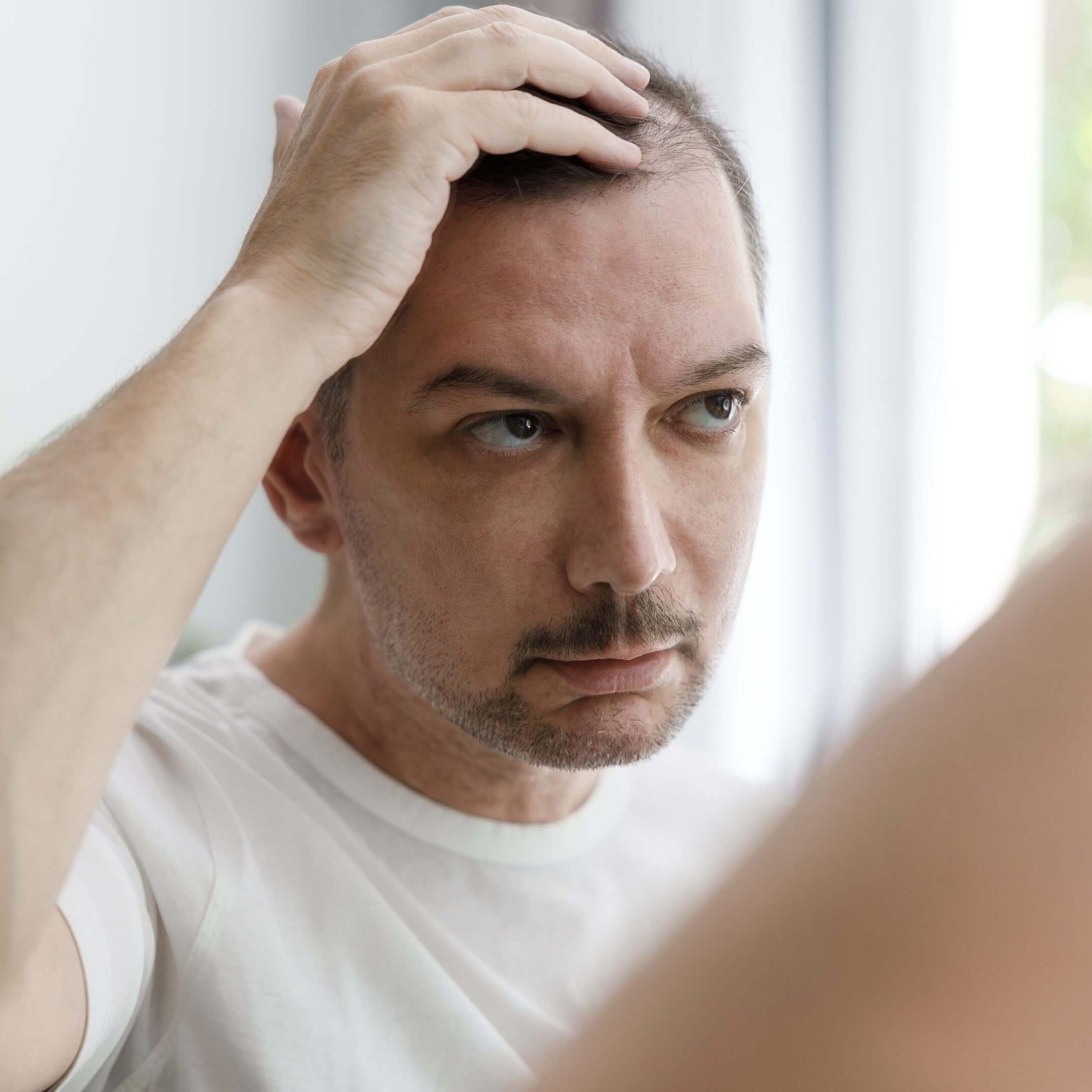 Man examining hair in bathroom mirror.